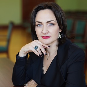 Dr. Eglė Vaidelytė sits at the table, sitting up straight, wearing a black jacket, her hand resting on her chin. She is the chief researcher of the project, a professor.