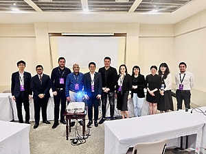 In 2025, ICPP7 participants, a group of 11 people, stand in a room with a screen in the background. Among them is project researcher Vytautas Valentinavičius.